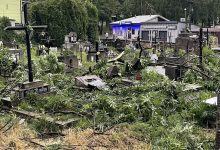 cmentarz i zniszczone nagrobki, przeszła nawałnica, duży wiatr. W oddali widać drzewa, bloki i niebo