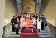 Członkowie klubów seniora pozują do wspólnego zdjęcia na reprezentacyjnych schodach budynku, trzymając czerwony baner z napisem „Gmina Dębno”; część osób trzyma kwiaty i upominki.